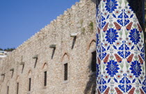 Architectural detail of pillar decorated with tiles painted with stylised floral design.  Length of fortified stone wall beyond.TurkishAegeancoastresortsummersunshineearly summer seasonMediter...