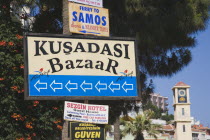 Signs for ferry  Kusadasi Bazaar and hotel with clock tower part seen behind.TurkishAegeancoastresortSummersunshineearly Summer seasonholidaydestinationdestinations ElladaEuropeanSouthern...