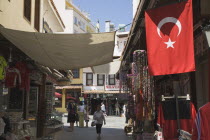 Open fronted shops with awning stretched across street above and Turkish flag hanging in the foreground.souvenirTurkishAegeancoastresortSummersunshineearly Summer seasonholidaydestinationDe...