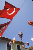 Turkish flags and colourful lanterns hanging across street from part seen buildings.TurkishAegeancoastresortSummersunshineearly Summer seasonholidaydestinationDestinations ElladaEuropeanSo...