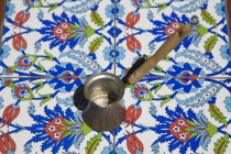 Turkish coffee pot standing on colourful tile with blue  green and red stylised floral design.TurkishAegeancoastresortSummersunshineearly Summer seasonholidaydestinationdestinations ElladaE...