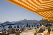 Lines of sun loungers and blue sun umbrellas for hire on beach  early morning with striped yellow and orange sun umbrellas in foreground.Turkish RivieraresortholidayDestinationholidaymakersparas...
