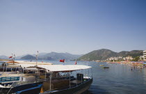 Marmaris on the Turkish Riviera in early summer season.  Moored ferry boats  with resort and busy beach in the background.coastcoastalseafrontwaterfrontholidayholidaymakerssunviewblue skycle...
