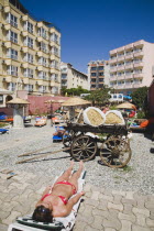 Marmaris on the Turkish Riviera in early summer season.  Tourists sunbathing in garden of resort hotel with display of traditional Turkish farm implements  tools and carts. coastcoastalresortholid...