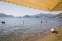 Marmaris on the Turkish Riviera in early Summer season Children playing on beach with tourists in water behind.  From shade of yellow parasol in early morning sun.coastcoastalresortfamilyseafront...