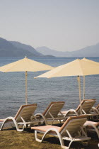 Parasols and sunbeds for hire on clean swept early morning beach with flat  calm water behind.Turkish RivieracoastcoastalresortsunshineholidaydestinationDestination Destinations European Mid...