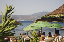 Parasols and sunbeds for hire on beach with views over bay on clear bright early Summer day with tourists looking out over calm  flat sea.formerly Greek Physkos in Caria once host to AlexandeTurkish...