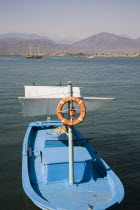 Olu Deniz.  Blue painted fishing boat with small life buoy and sun shade with Turkish Riviera coast and gulet beyond.AegeancoastcoastalOludeniz Destination Destinations European Middle East Turkiy...