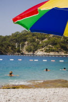 Olu Deniz.  Tourists swim at entrance to lagoon and beach rated in top five worldwide.  Part seen brightly coloured parasol in foreground.Turkish rivieraAegeancoastcoastalOludenizseashorecalm...