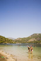 Olu Deniz.  Turkish female tourists in Western style bikini  swimwear walking through clear  shallow water towards shore with tree covered coastline behind.Turkish rivieraAegeancoastcoastalOluden...