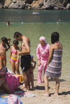 Olu Deniz.  Turkish family at the beach with woman in pink Burkini Muslim swimwear and children in bikinis.Turkish rivieraAegeancoastcoastalOludenizseashorecalmclearshallowazurebrightsun...