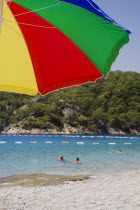 Olu Deniz.  Tourists swim at entrance to lagoon and beach rated in top five worldwide.  Part seen brightly coloured striped parasol in foreground.Turkish RivieraAegeancoastcoastalOludenizseasho...