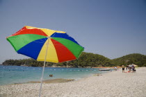 Olu Deniz.  Tourists swim at entrance to lagoon and beach rated in top five worldwide.  Brightly coloured striped parasol in foreground.Turkish RivieraAegeancoastcoastalOludenizseashorecalmcl...