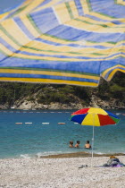 Olu Deniz.  Tourists swim at entrance to lagoon and beach rated in top five worldwide.  Brightly coloured striped parasol on shore and part seen blue and yellow parasol in immediate foreground.Turkis...