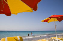 Red and yellow striped parasols and yellow and white sun loungers on Ixia beach resort looking north towards Turkish coast.  Tourists standing in clear  aquamarine sea and breaking surf.Aegeancoast...