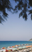 Ixia beach with view across lines of parasols and sunbeds part framed by branches of pine trees in early Summer season.Aegeancoastcoastalformer Ottoman territorylocation for Guns of NavaroneRodi...