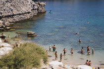 Looking down on Lindos beach with tourists swimming and standing in clear  shallow  aquamarine water sheltered by cliffs. AegeancoastcoastalFormer Ottoman territorysunshineearlySummer seasonpa...