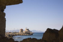 Rhodes Town.  View from the St Pauls Gate entrance to the Old Town across water towards circular stone windmills with masts of fishing boats behind.  Part framed by silhouetted rocks.Aegeancoastcoa...