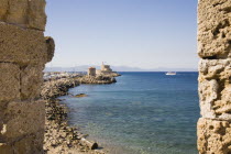 Rhodes Town.  View from the St Pauls Gate entrance to the Old Town across water towards circular stone windmills with masts of fishing boats in harbour behind.  Part framed by ancient stone walls.Aeg...
