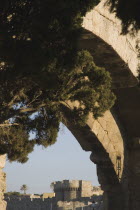 View towards crenellated walls and fortified towers of the St Catherines gate entrance to the Old Town framed by stone arches and tree branches.Aegeancoast  coastalFormer Ottoman territoryearly S...