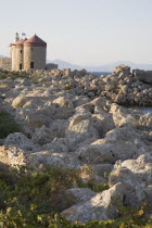 Old Town  Mandraki Harbour.  Medieval stone windmills on the pier in clear late afternoon sun with scattered  eroded rocks used as sea defences in the foreground.Aegeancoast  coastalFormer Ottoman...