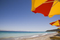 Ixia beach outside Rhodes Town.  Part seen red and yellow sun umbrellas on beach in late afternoon sun on perfect clear day.GreekAegeanCoast - CoastalRodiPackage holidaydestination resortsun su...