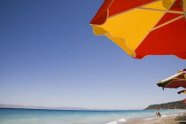 Ixia Beach outside Rhodes Town.  Part seen red and yellow striped sun umbrellas against cloudless blue sky in late afternoon sun in early summer season.GreekAegeanCoast - CoastalRodiPackage holid...