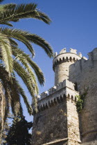 Old Town crenellated city walls and tower with fronds of palm tree in foreground against cloudless blue sky.GreekAegeanCoast - CoastalRodiPackage holidaydestination destinations resortsun sunsh...