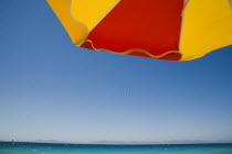Ixia beach resort outside Rhodes Town popular for water sports  with striped red and yellow sun umbrella against backdrop of cloudless blue sky and distant Turkish coast on bright Summer morning.Aege...