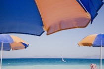Ixia beach resort popular for water sports with part seen blue and orange striped sun umbrellas in foreground against blue  cloudless sky and sea view with distant windsurfer.AegeanRodiseacoast co...