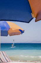 Ixia beach resort popular for water sports with line of blue and orange striped sun umbrellas and sun lounger in foreground against blue  cloudless sky and sea view with windsurfer behind.AegeanRodi...