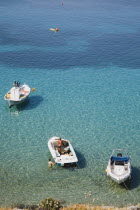 Lindos.  View over clear  shallow  aquamarine water of bay with boats moored in the foreground and tourists in late afternoon sunshine.Greek IslandsAegeanRodicoast coastalsearesortholidaypacka...