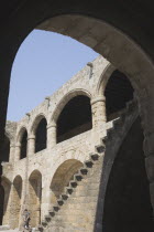 Figure at foot of flight of stone steps with covered colonnades framed by archway in foreground.AegeanGreek IslandsRhodiSummercoast coastalresortholidaypackagetripDestination Destinations El...