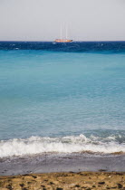 Rhodes Town.  Town beach with view across expanse of turquoise water towards day trip cruise boat returning home.AegeanGreek IslandsRhodiSummerseacoast coastalresortholidaypackagetripDestin...