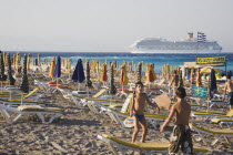 Rhodes Town.  Young Greek boys playing paddle ball amongst striped parasols and sunbeds on Rhodes Town beach with cruise ship on horizon behind.AegeanGreek IslandsRhodiSummerseacoast coastalres...