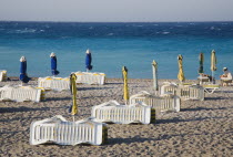 Rhodes Town.  Lines of rental sunbeds and parasols packed up and folded on town beach at the end of the day with expanse of clear  aquamarine water behind in late afternoon sunshine.AegeanGreek Isla...