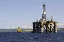 Scotland, Invergordon, Oil Rig Platform being pulled out to sea by tug vessel.ScotsWaterSeaOceanOilPetrolPetroeumRigPlatformDerrickDrillDrillingIndustryBoatShipBlue Ecology Entorno En...
