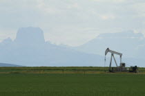 Nodding donkey oil derrick against the Rockies and Chief Mountain.American Canadian North America Northern Blue Clouds Cloud Sky Ecology Entorno Environmental Environnement Green Issues Scenic
