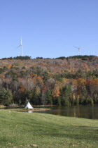 Wind generators on hill top above field with traditional Teepee next to lake. Colourful Autumn trees.windmills  wind energy  teepeeAmerican North America Northern United States of America Blue Classi...
