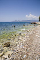 Pythagorio.  Tourists in shallows of clear water on pebble beach with South West coast of island in distance behind.AegeanGreek IslandsPythagorionSummerseacoast coastalresortholidaypackagetr...