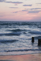 Kusadasi.  Shoreline at sunset looking west to nearby Greek island of Samos with pale pink sky reflected in wet surface of sand.waveshallowreflectioncloudeveninglighttwilightdusk Blue Destinat...