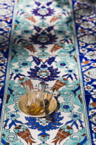 Kusadasi.  Empty Turkish coffee glass on blue  red and turquoise tiled surface at Club Caravanserail built by vizier Okuz Mehmed Pasha in 1618 for the Ottoman Sea trade.  Restored in 1966  now used as...