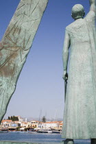 Pythagorio.  Statue of the philosopher and mathematician Pythagoras on waterfront with diagrams on angled plinth alongside framing view across harbour to line of waterfront buildings beyond.AegeanGr...