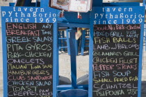 Pythagorio.  Menu on chalkboard on waterfront in English with typical blue Greek island decor.AegeanGreek IslandsPithagorion Pythagorioncoast coastalseaSummerpackageholidayresortvacationtri...