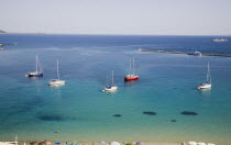 Pythagorio.  Yachts moored in the bay with tourists swimming in clear  aquamarine water in early Summer season and line of parasols along beach partly seen in foreground.North Eastern AegeanGreek Is...