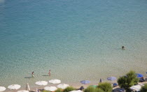 Pythagorio.  Tourists in early Summer season in clear  shallow  aquamarine water of bay with line of parasols on the beach part seen in foreground.North Eastern AegeanGreek IslandsPithagorion Pytha...