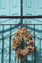 Pythagorio.  Flower wreath in memory of deceased family member hanging from decorative metal work casting shadow on front of turquoise painted window shutter of traditional Greek house.North Eastern...