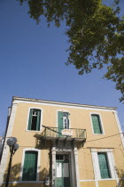 Pythagorio.  Yellow and white painted facade of restored house with green window shutters against blue sky on clear  late afternoon in early Summer.North Eastern AegeanGreek IslandsPithagorion Pyth...