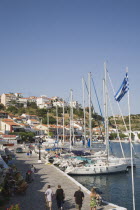 Pythagorio.  Tourists walking along waterfront beside line of moored rental yachts in late afternoon in early Summer with view towards town houses on hillside beyond.North Eastern AegeanGreek Island...