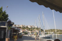 Pythagorio.  Tourists walking along waterfront beside line of moored rental yachts in late afternoon in early Summer with view towards town houses on hillside beyond.North Eastern AegeanGreek Island...